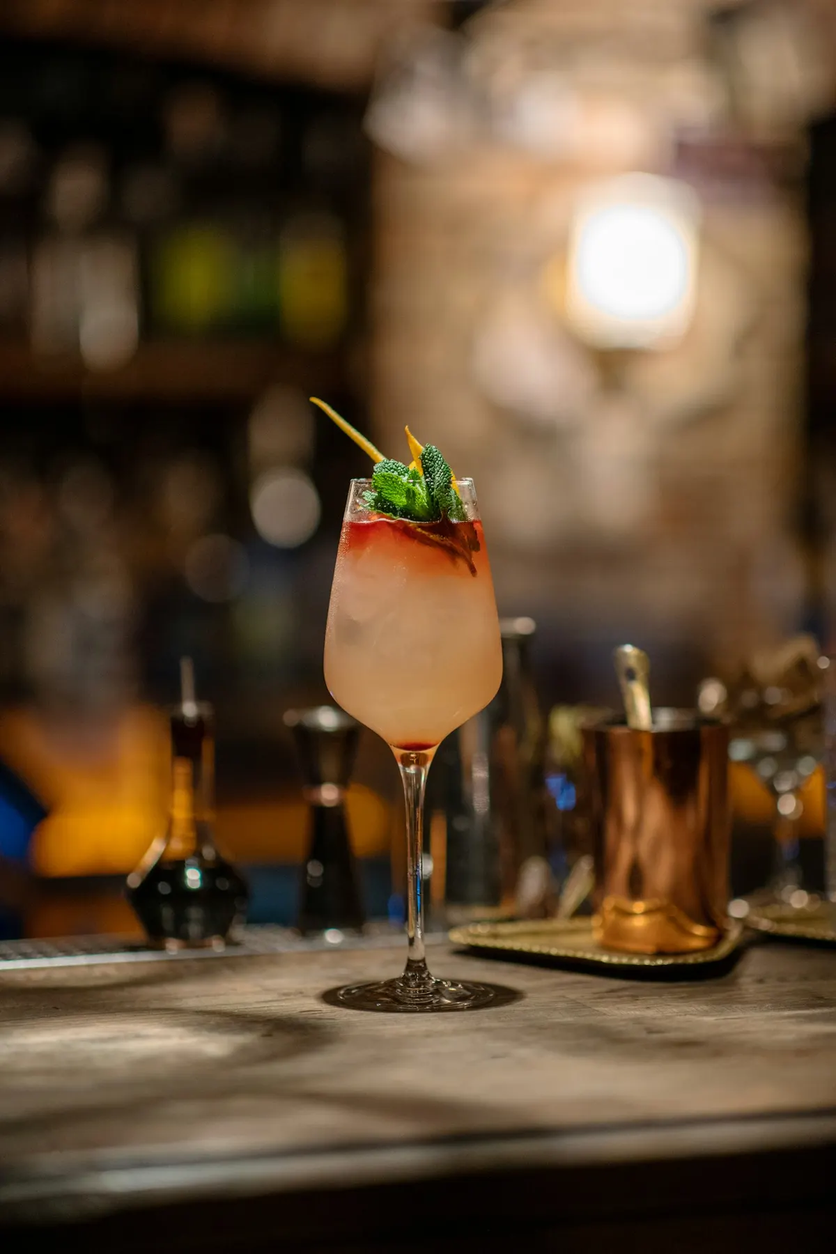 A garnished cocktail on a wooden bar top in warm low light