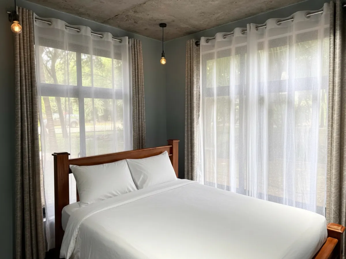 A garden room bedroom dressed in white linen, with garden light through sheer curtains