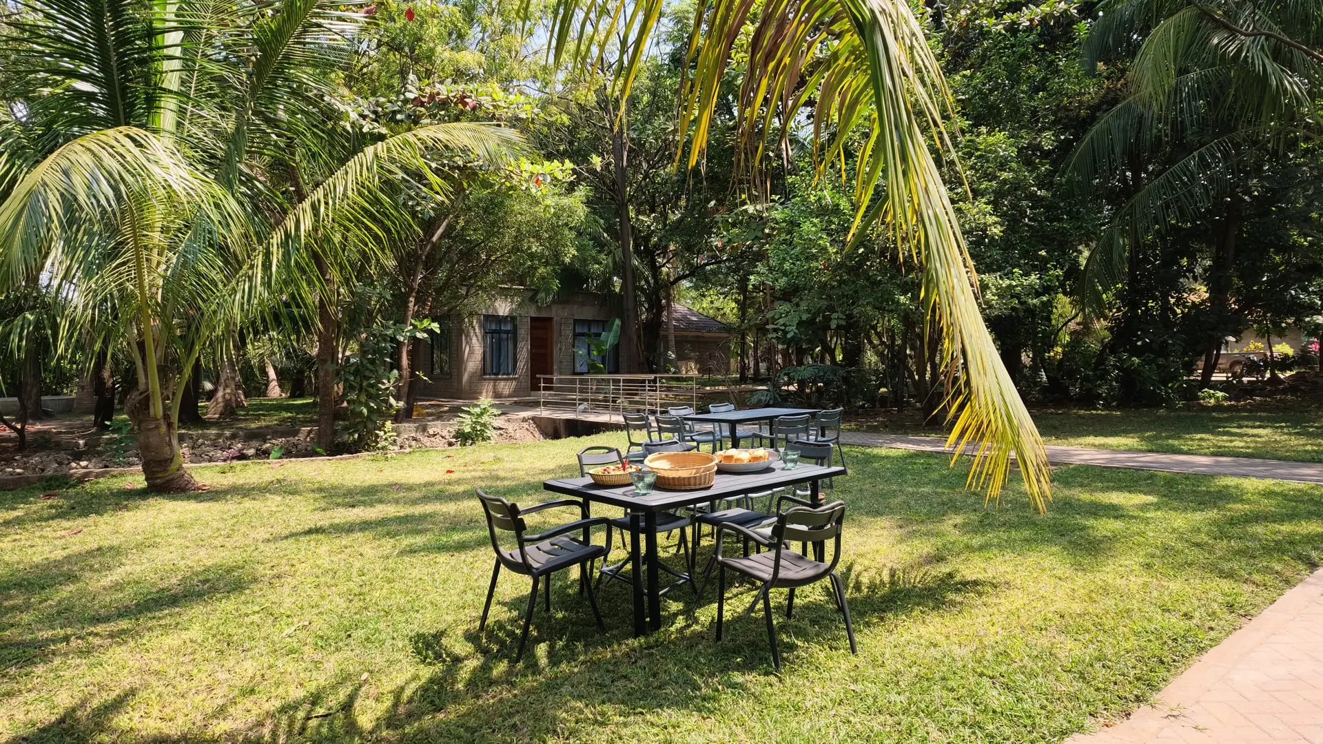 Tables laid for a meal on the lawn at Nagira, shaded by coconut palms with the restaurant building behind